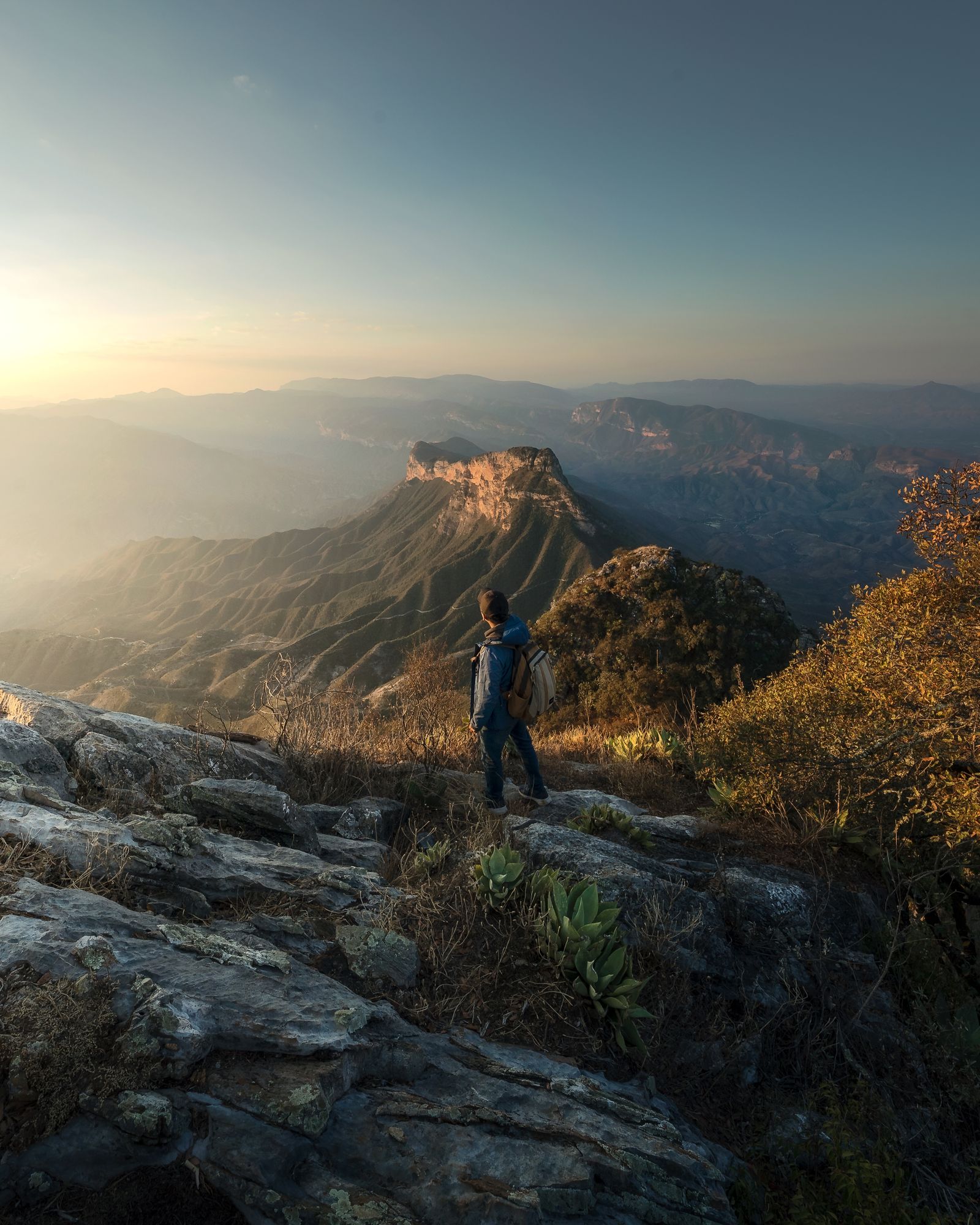 A hiker looking out over a mountain range at sunrise